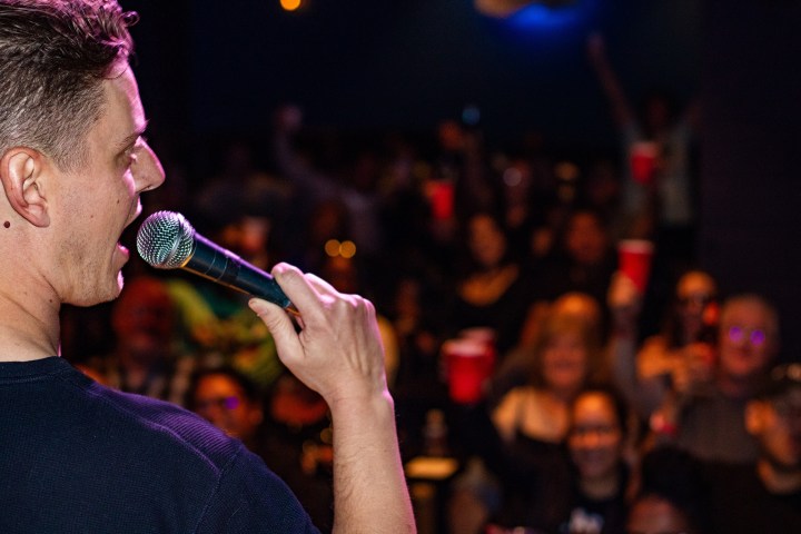 Person holding microphone facing a cheering crowd with red cups.