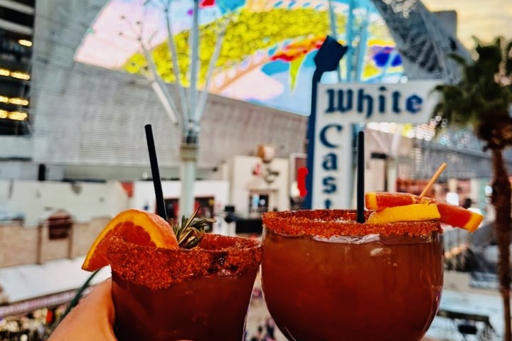 Hands holding drinks with a colorful display and city buildings in the background.