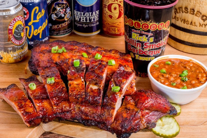 Sliced barbecue ribs on a board with baked beans and assorted beer cans.