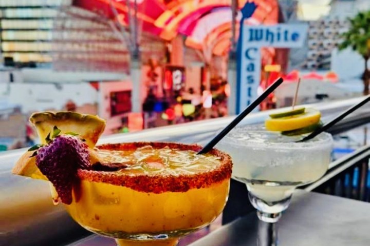 Two cocktails on a rooftop with colorful city lights in the background.