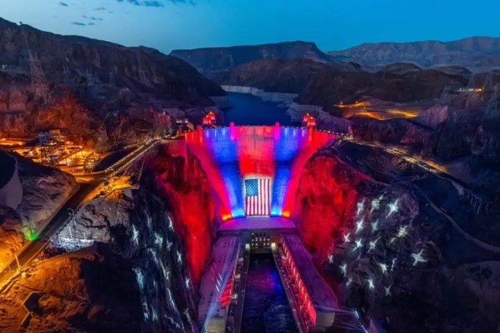 Hoover Dam lit with red, white, and blue lights at dusk.