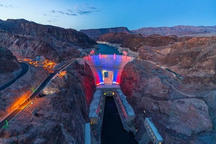 Aerial view of illuminated dam with American flag at twilight.