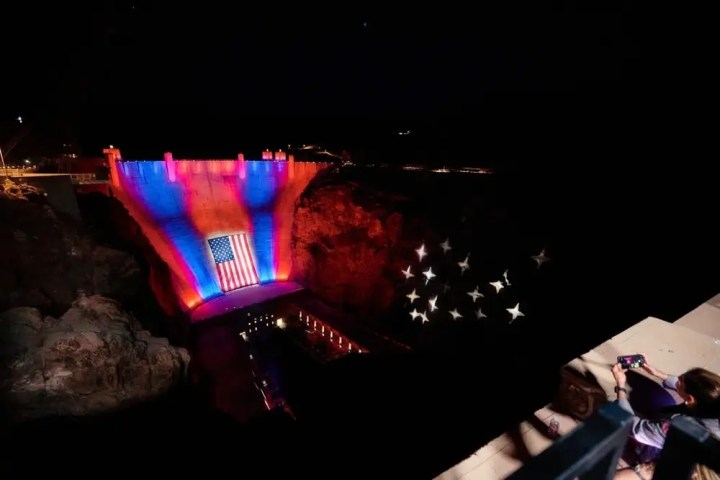 Hoover Dam illuminated with American flag and stars at night.