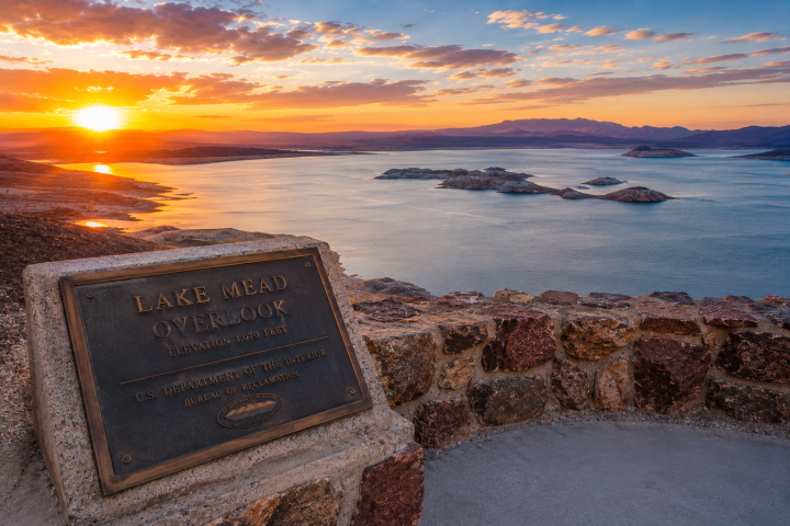 Sunset view of Lake Mead with a plaque reading 'Lake Mead Overlook' in the foreground.